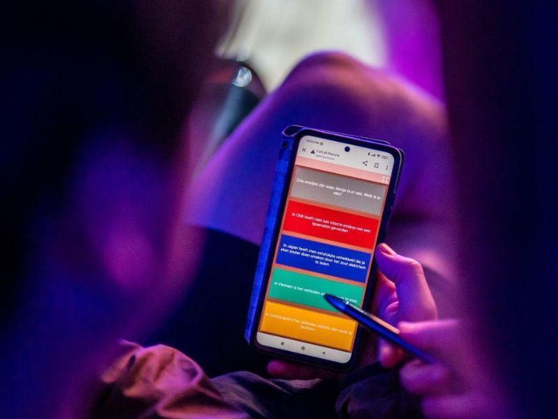 A picture of a contestant holding a smartphone and selecting a multiple choice answer.